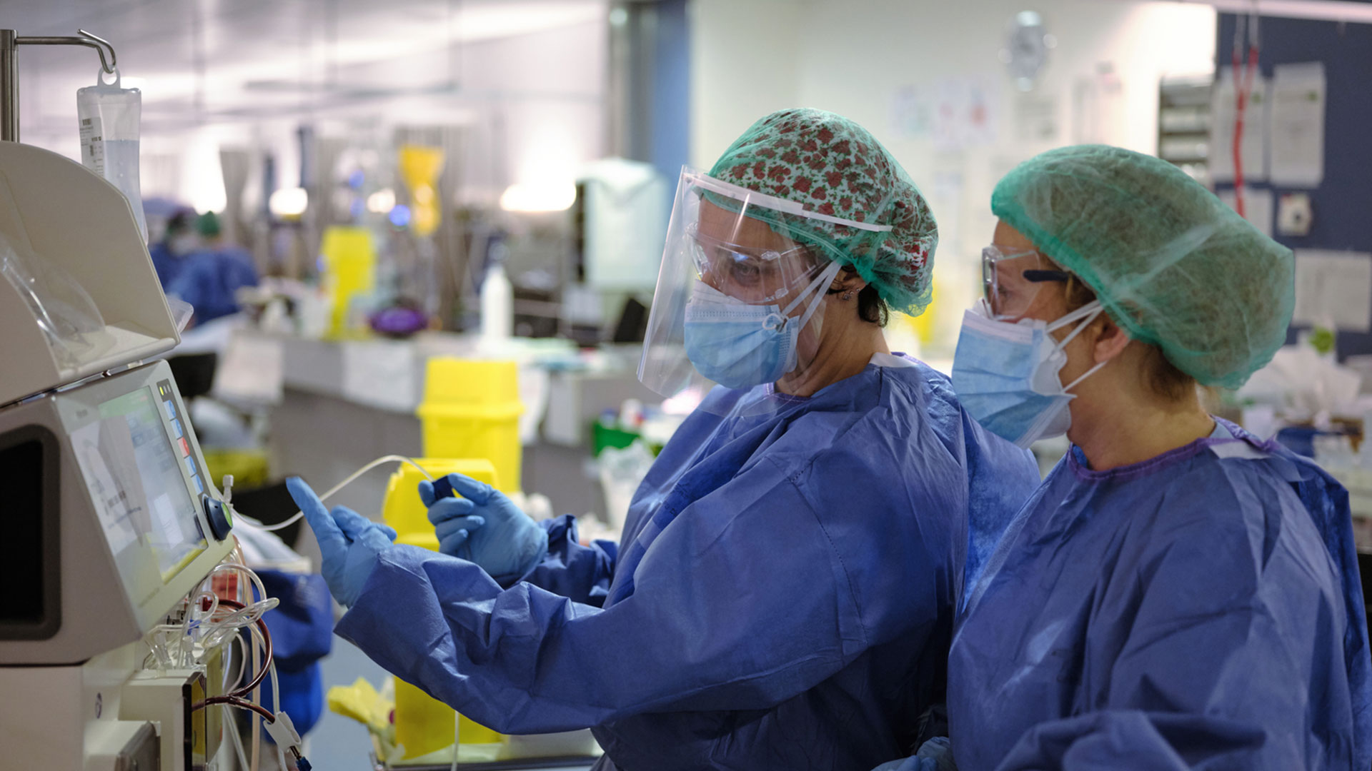 doctor and nurse with face mask scrubs and shield looking at cardiology device and analyzing data