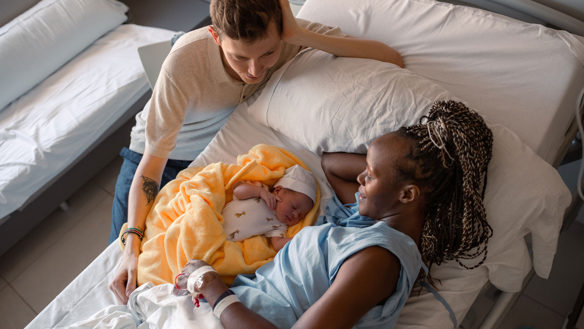 black woman laying on hospital bed looking at her newborn child husband sitting next to bed