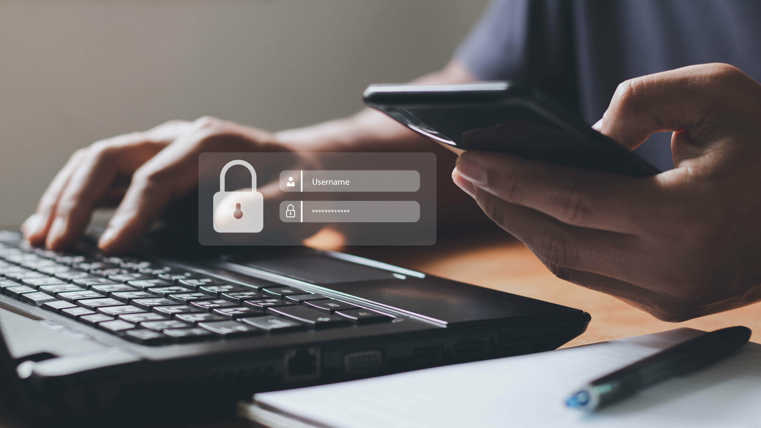 man trying to login to account through a phone in front of laptop