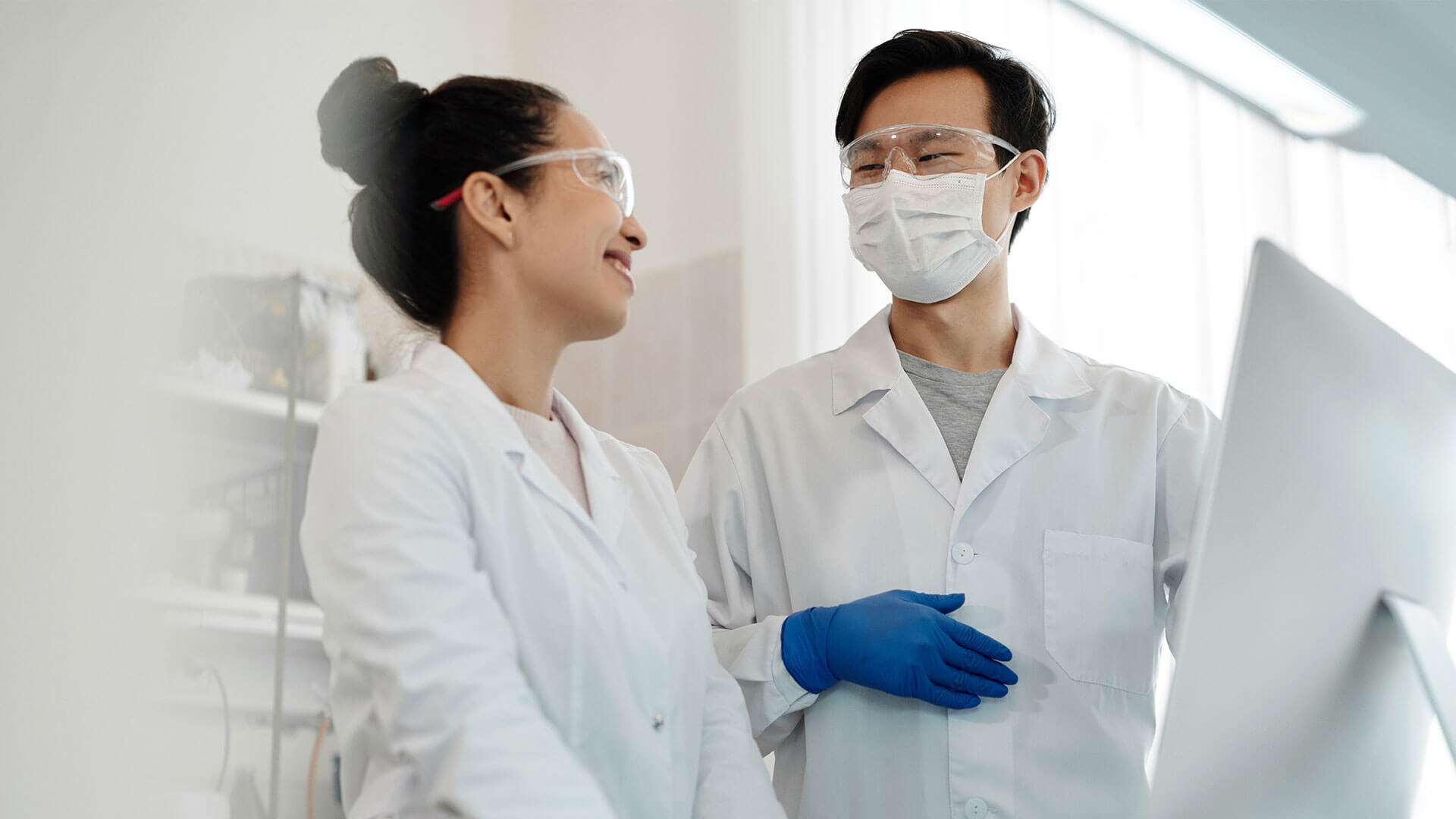 male scientist wearing mask and pointing at computer screen during discussion with female colleague