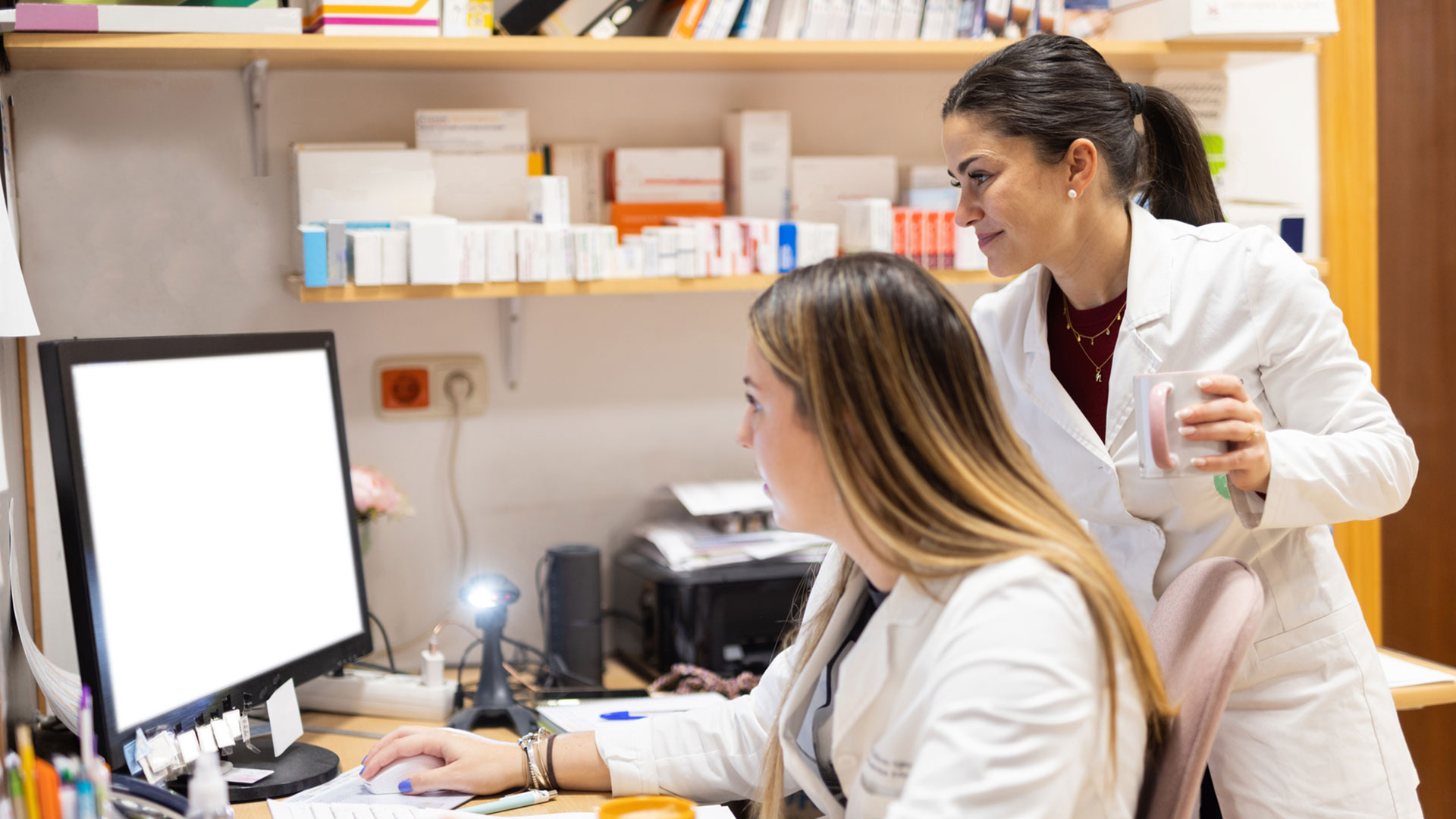 two woman researchers with white scrubs collaborating on computer