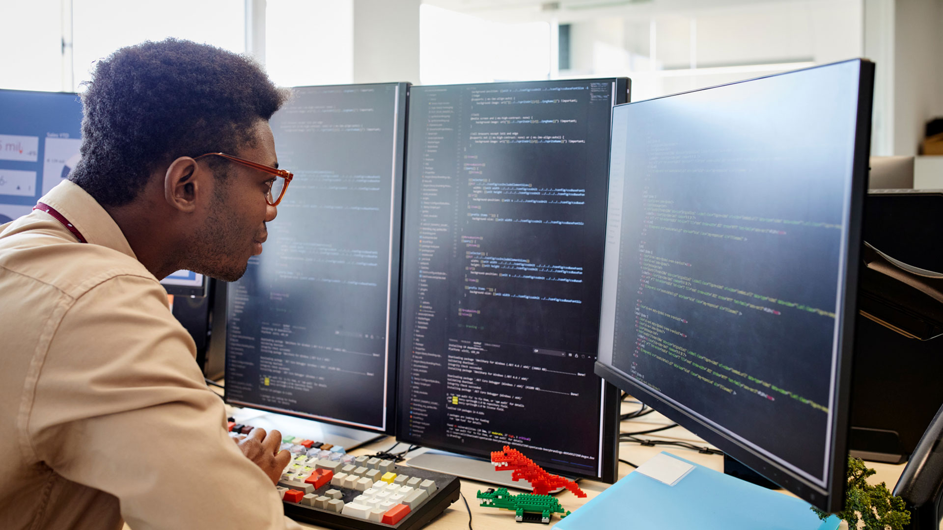 young male research analyst sitting in front of four computer screens reviewing code