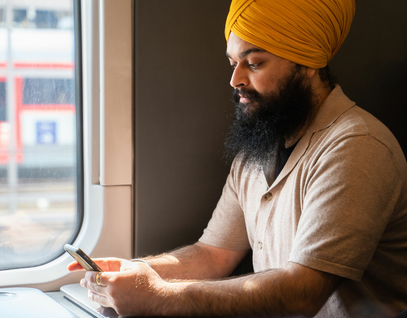 man sitting on public transit typing on his mobile device