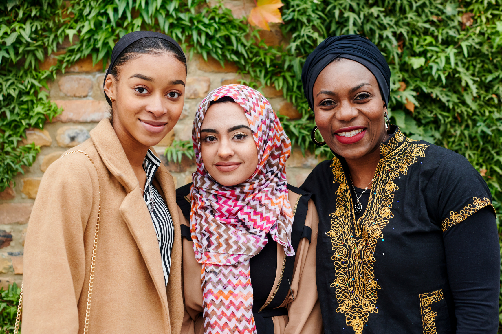 Diverse group of smiling Muslim women standing together outside in front of a brick wall in a park
